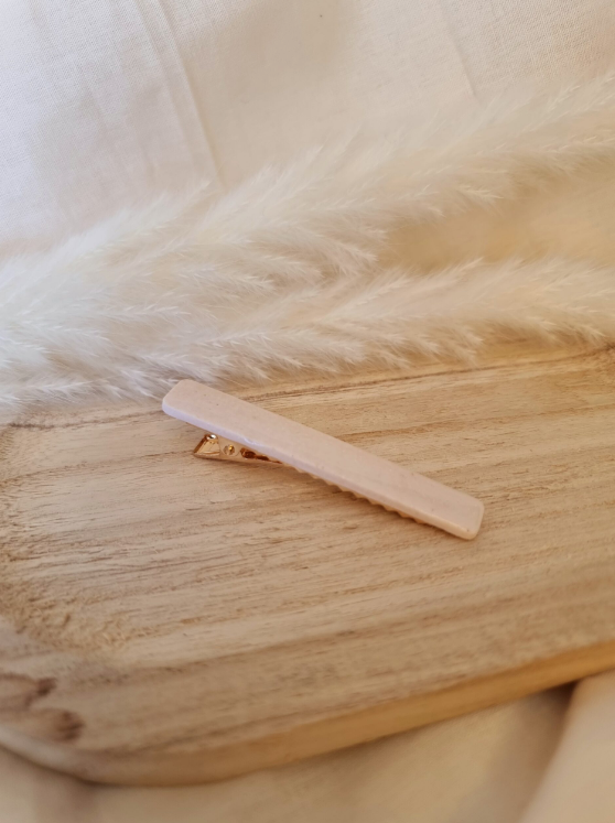 Barrette de forme rectangulaire posée sur un support en bois. Faite main en argile polymère et en acier inoxydable. Ton blanc. Modèle Barrette Fine, style classique.