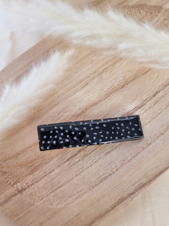 Barrette de forme rectangulaire posée sur un support en bois. Faite main en argile polymère et en acier inoxydable. Tons noir et blanc. Modèle Barrette Fine, style classique.