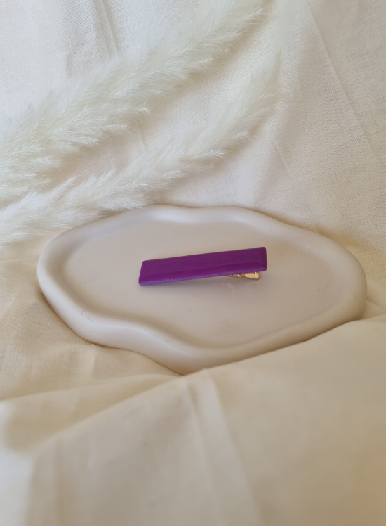 Barrette de forme rectangulaire posée sur un support en bois. Faite main en argile polymère et en acier inoxydable. Ton violette. Modèle Barrette Fine, style classique.