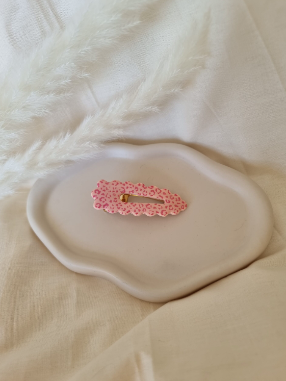 Barrette de forme triangulaire posée sur un support céramique blanc. Faite main en argile polymère et en acier inoxydable. Tons rose. Modèle Barrette Fleurie, style classique.