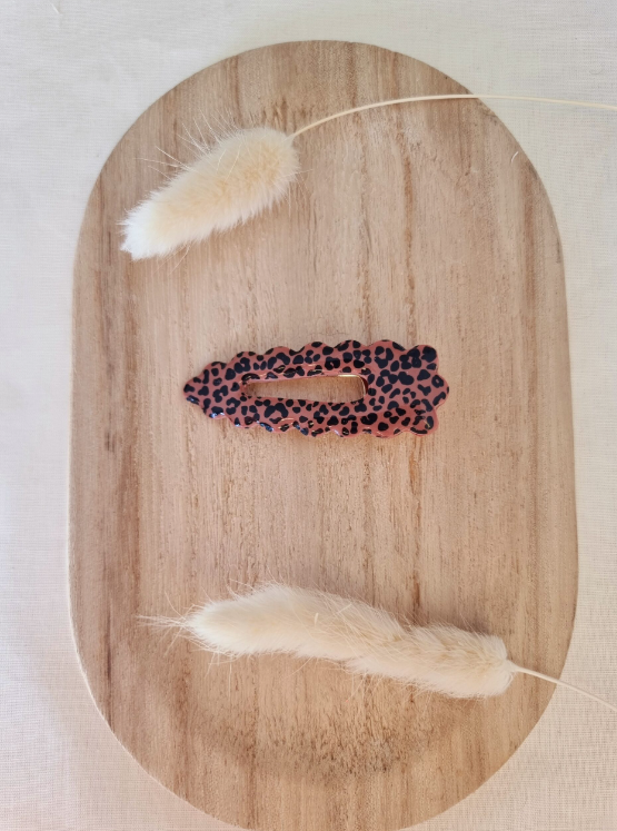 Barrette de forme triangulaire posée sur un support en bois entouré de fleurs. Faite main en argile polymère et en acier inoxydable. Ton leopard. Modèle Barrette Fleurie, style classique.