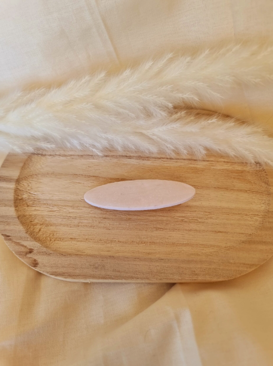 Barrette de forme ovale posée sur un support en bois. Faite main en argile polymère et en acier inoxydable. Ton blanc. Modèle Barrette Ovale, style classique.
