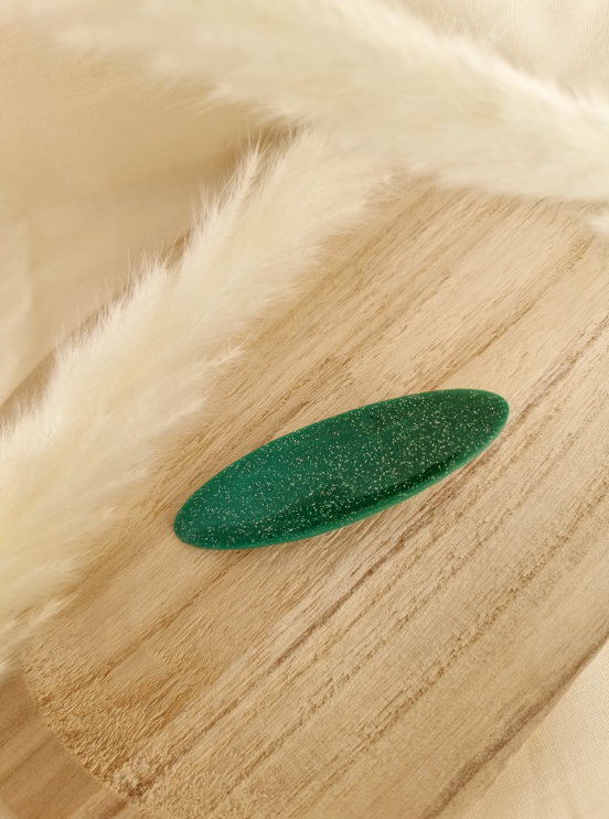 Barrette de forme ovale posée sur un support en bois. Faite main en argile polymère et en acier inoxydable. Ton turquoise. Modèle Barrette Ovale, style classique.