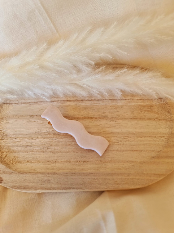 Barrette en forme de vague posée sur un petit plateau en bois. Faite main en argile polymère et en acier inoxydable. Ton blanc. Modèle Barrette Vague, style classique.