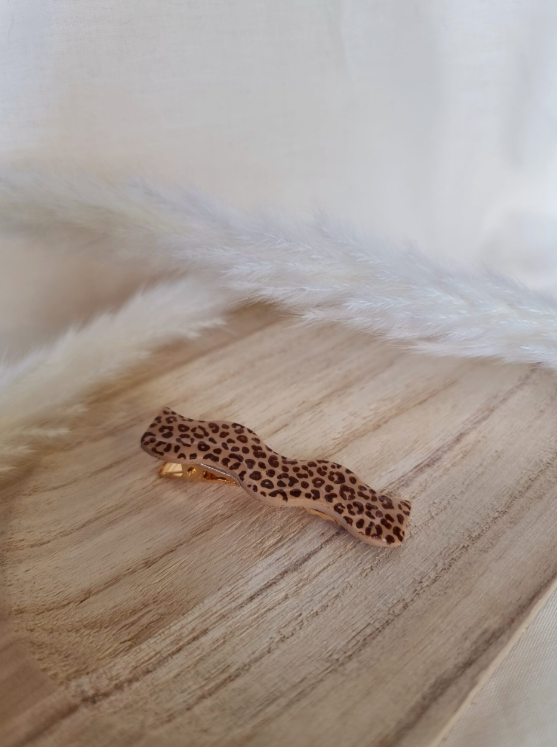 Barrette en forme de vague posée sur un petit plateau en bois. Faite main en argile polymère et en acier inoxydable. Ton léopard. Modèle Barrette Vague, style classique.