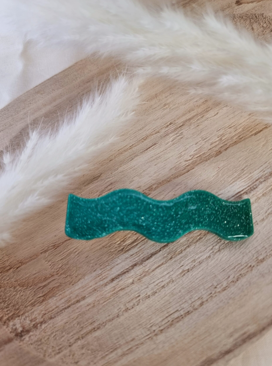 Barrette en forme de vague posée sur un petit plateau en bois. Faite main en argile polymère et en acier inoxydable. Ton turquoise. Modèle Barrette Vague, style classique.