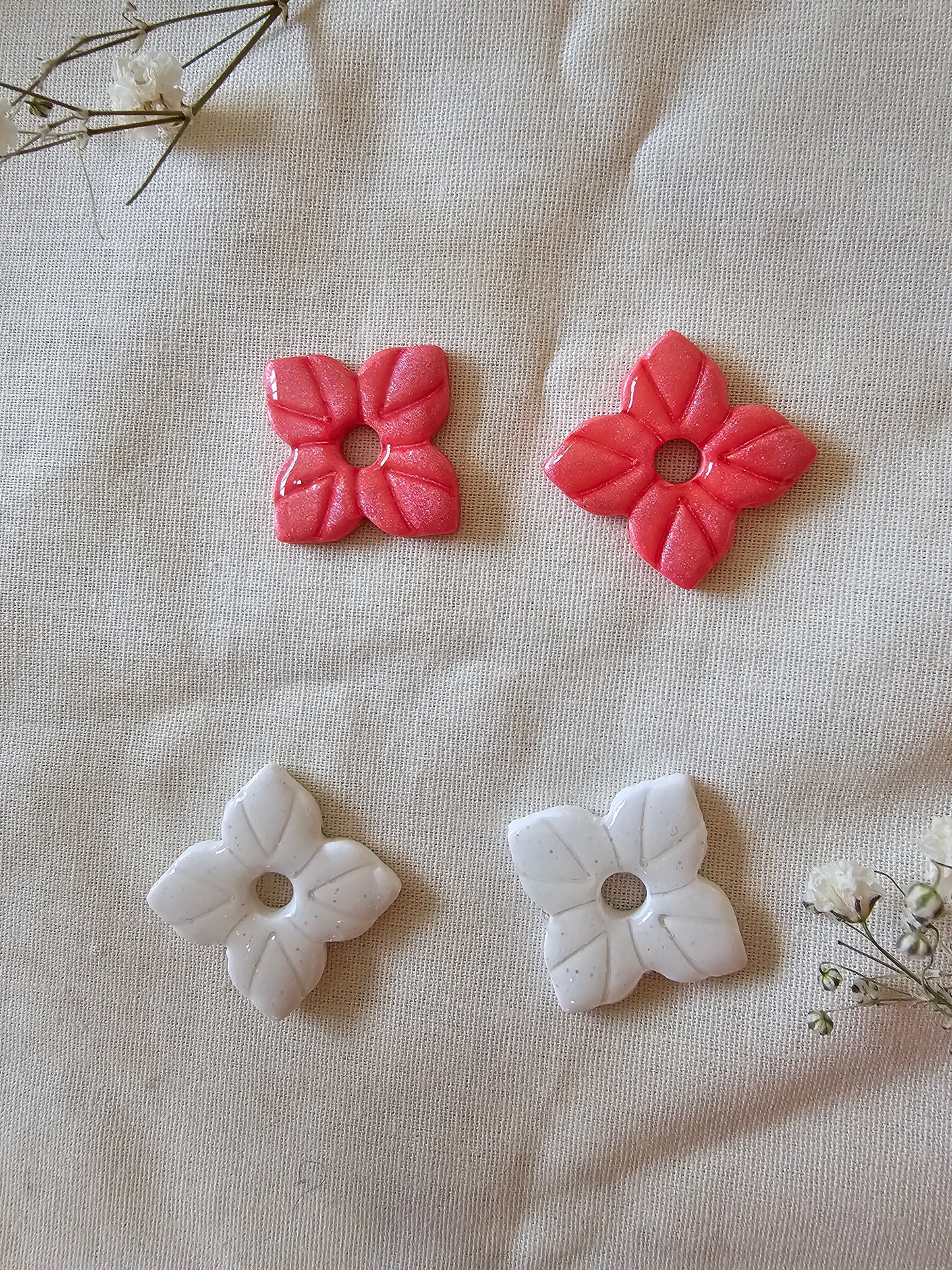 2 paires de pampilles en forme d'étoile, faites main en argile polymère, posées sur un tissu blanc cassé. Tons corail et blanc irisé. Prise de vue rapprochée. Modèle Anthéna, style floral et astral.