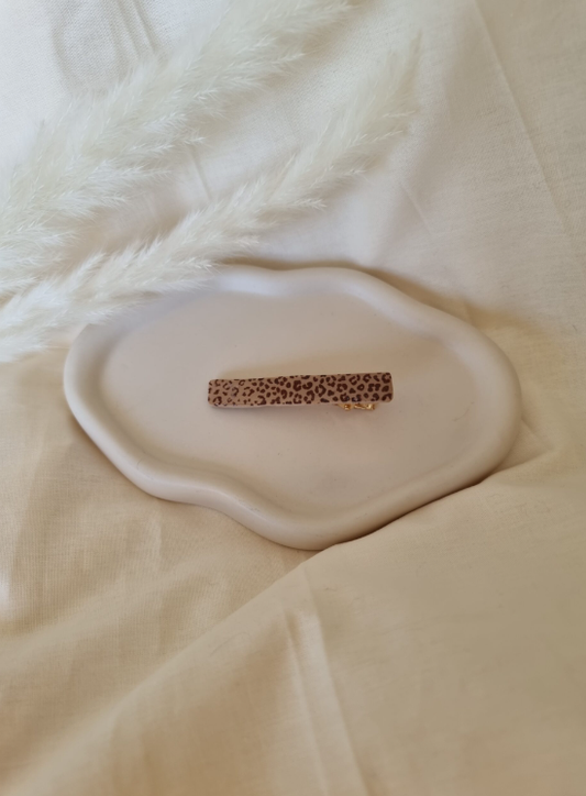 Barrette de forme rectangulaire posée sur un support en bois. Faite main en argile polymère et en acier inoxydable. Ton léopard. Modèle Barrette Fine, style classique.