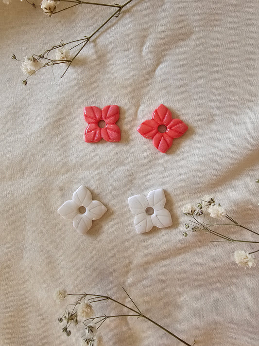 2 paires de pampilles en forme d'étoile, faites main en argile polymère, posées sur un tissu blanc cassé. Tons corail et blanc irisé. Prise de vue large. Modèle Anthéna, style floral et astral.